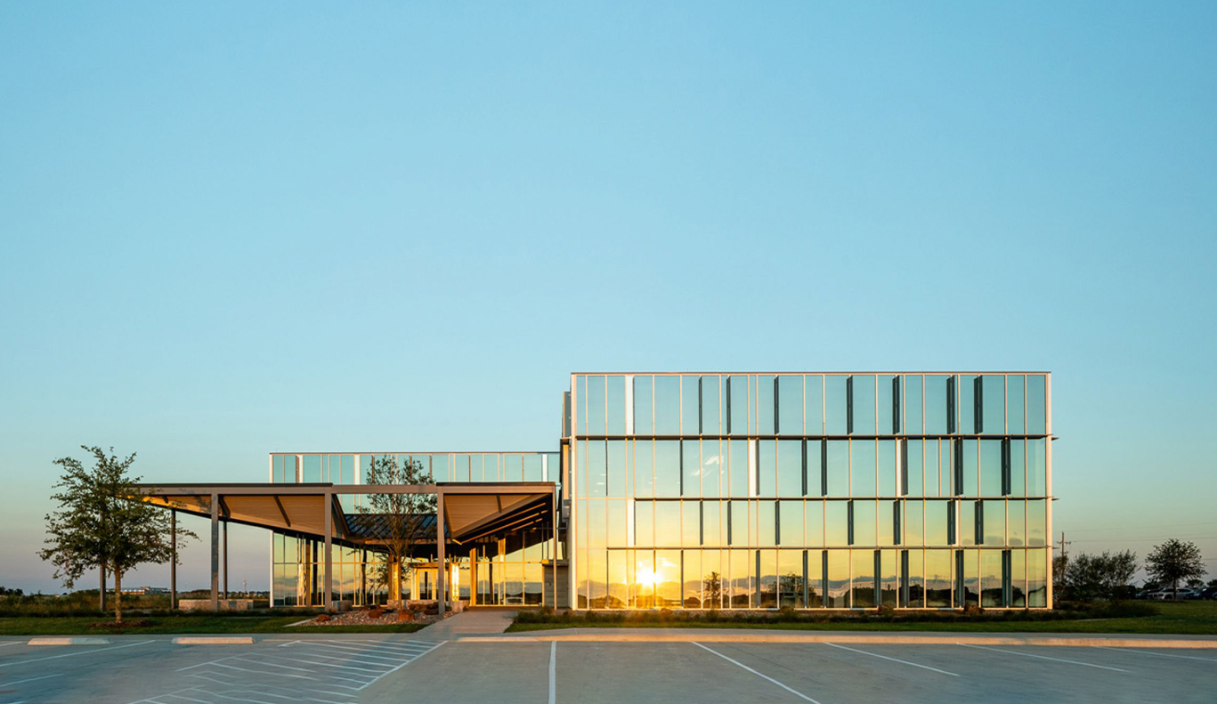 A glass office building with a parking lot in the background.