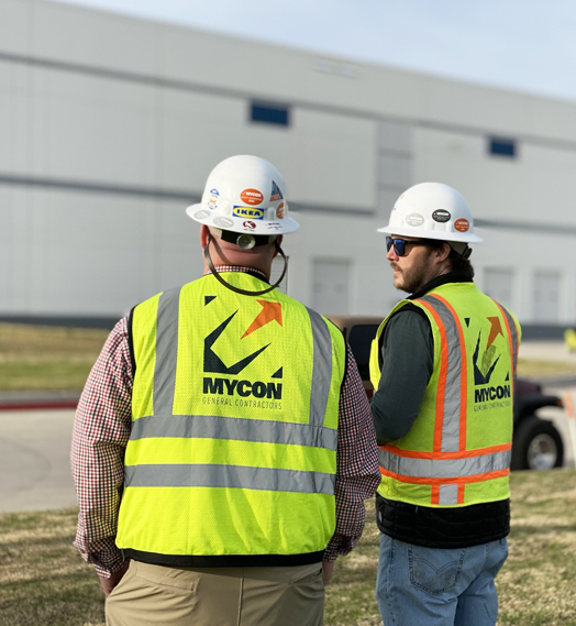 Two men in hard hats standing in front of a building.