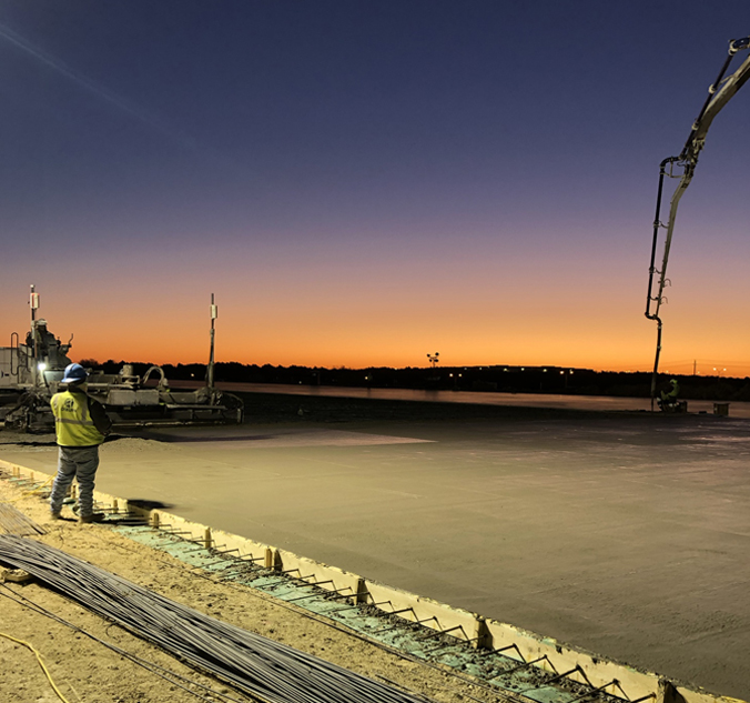 A worker is working on a concrete slab at dusk.