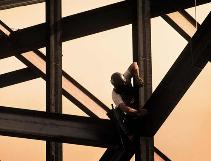 A worker is working on a steel structure at sunset.