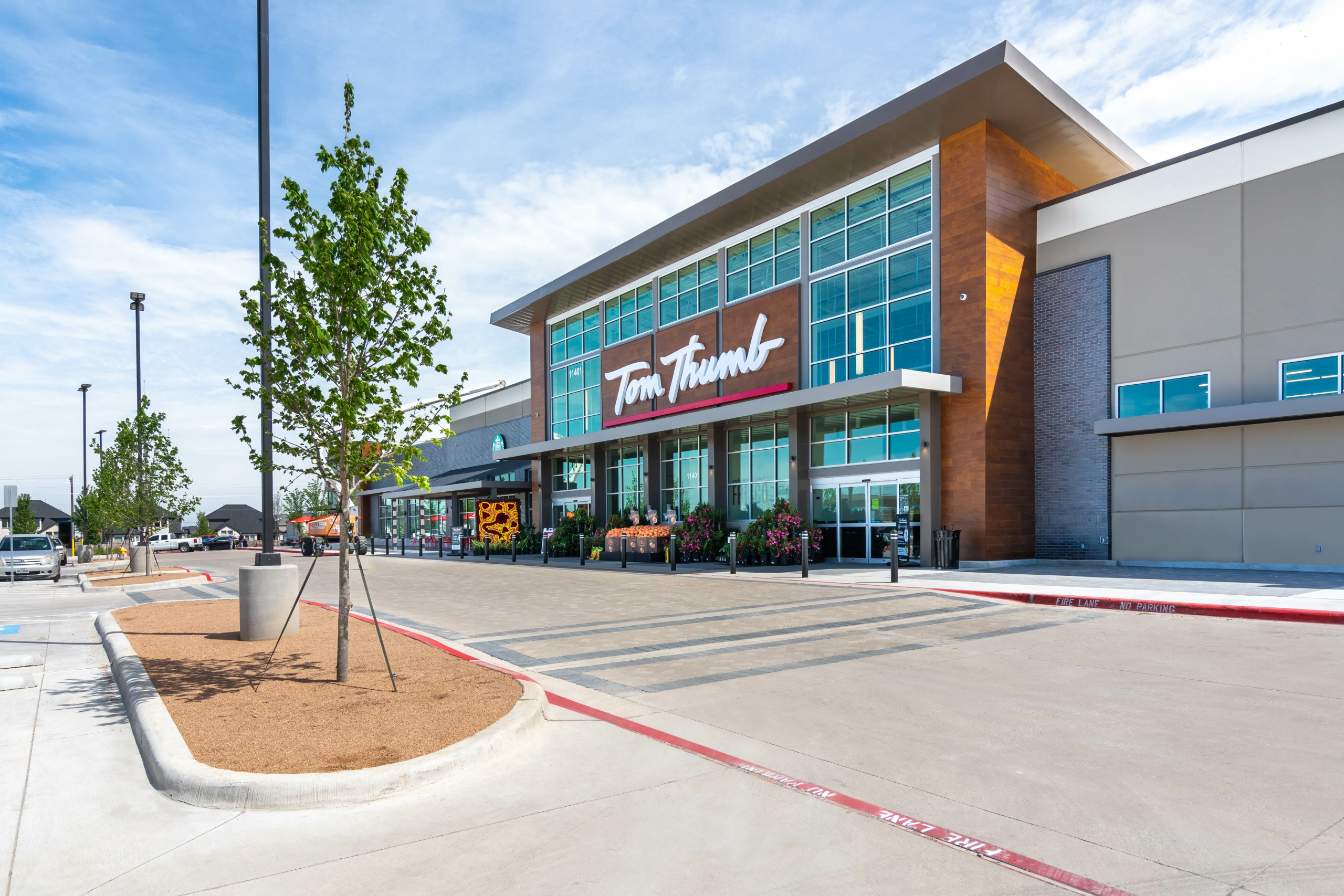 Exterior view of a modern tom thumb grocery store on a sunny day, featuring clear skies, a landscaped parking lot, and prominent store signage.