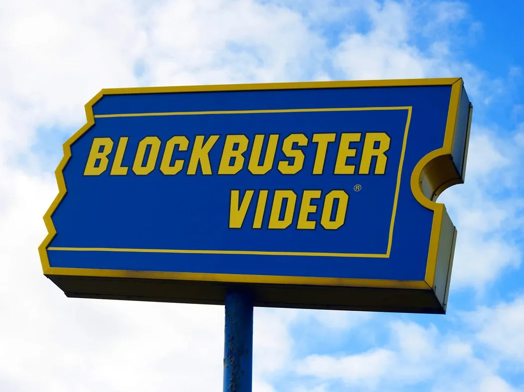 Blockbuster video is a blue and yellow sign in front of a blue sky.