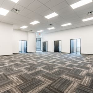 An empty office with gray carpeting and doors.