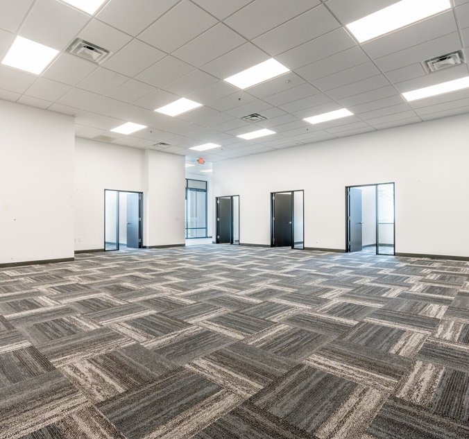 An empty office with gray carpeting and doors.