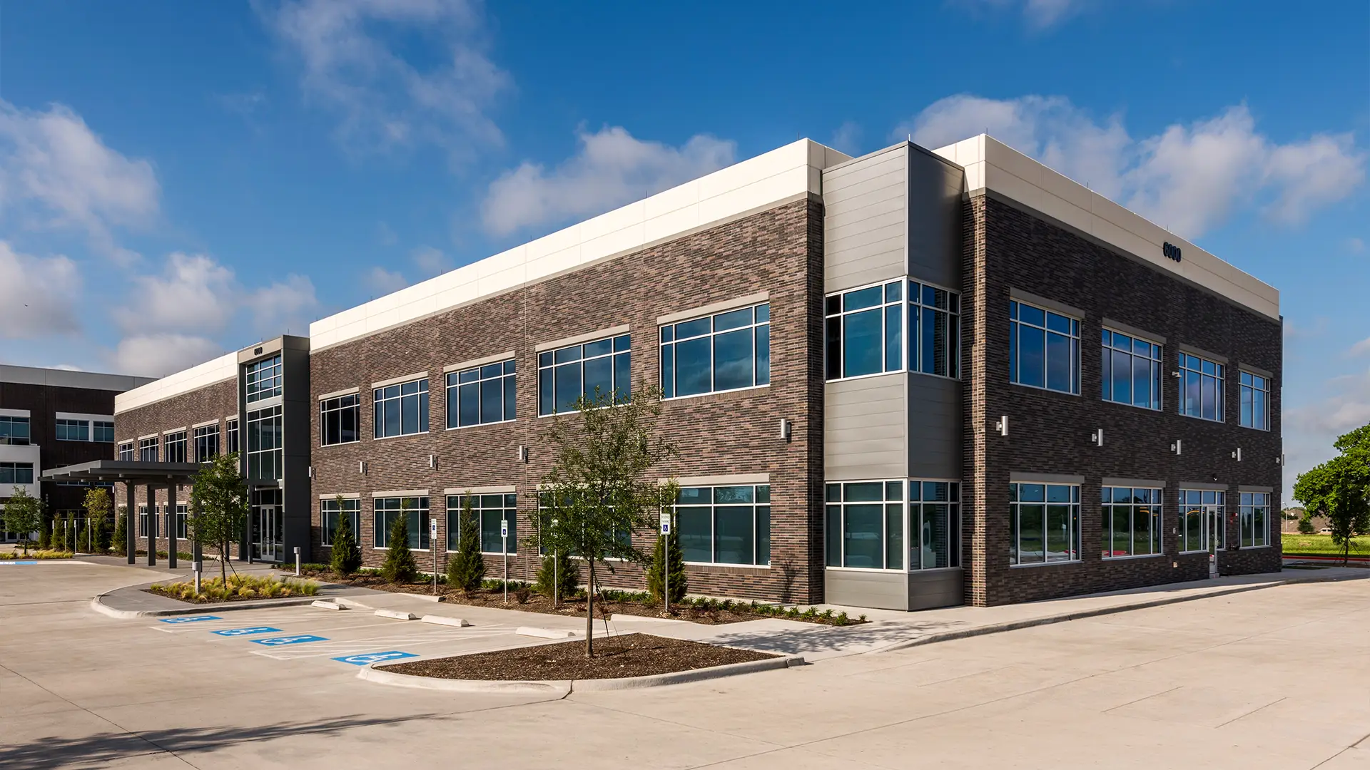 Two-story modern Spring Creek Medical Office Building with large windows, brick and metal exterior, surrounded by a parking lot with accessible spaces and landscaped grounds.