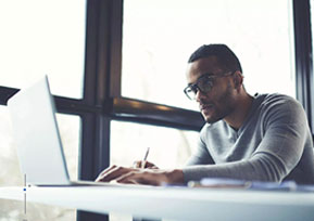 A man working on a laptop in front of a window.