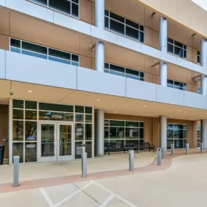 Exterior view of a modern medical building with large glass windows, automatic doors, metal columns, and the Holston Medical Group logo alongside Baylor Scott & White Medical Office Building signage on the upper right corner.