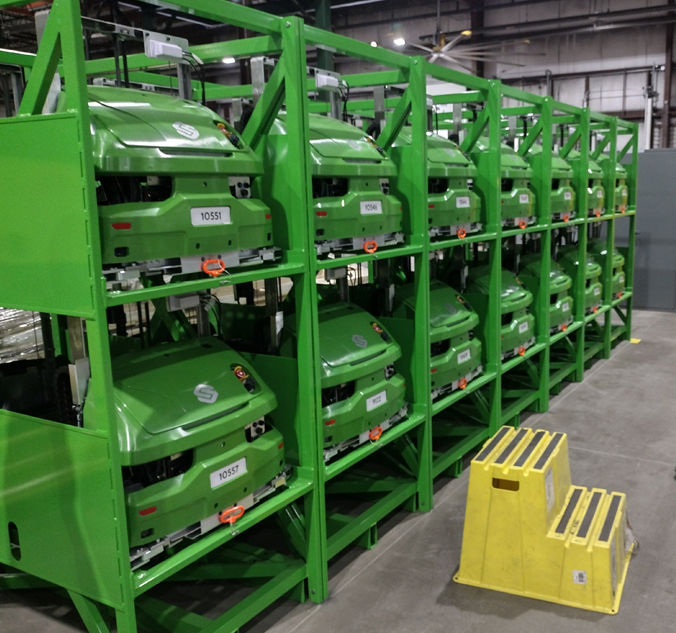 Green mowers on a rack in a warehouse.