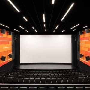 An auditorium with an orange screen and black chairs.
