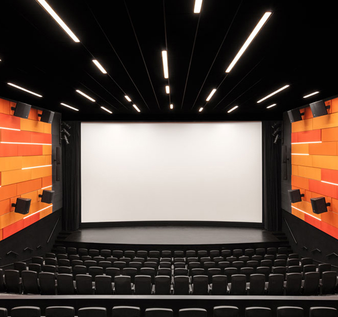 An auditorium with an orange screen and black chairs.