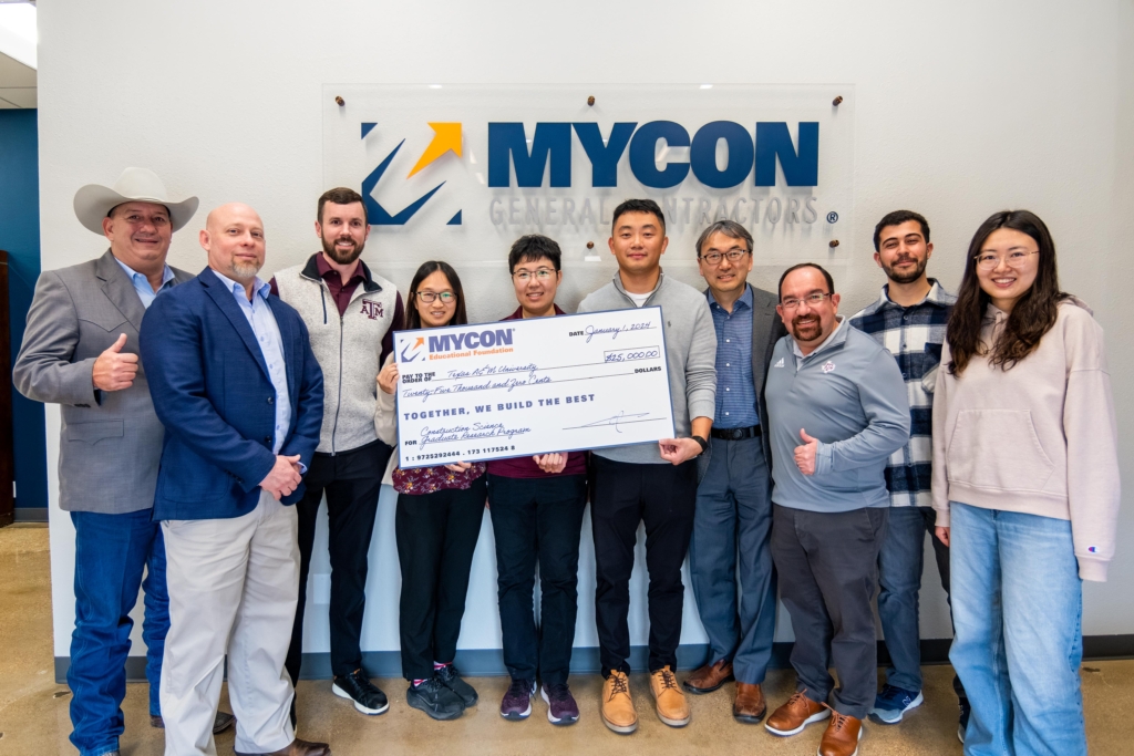 A group of people standing in front of a sign that says mycon.
