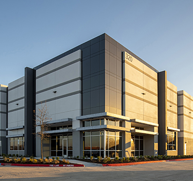 A large warehouse building in the middle of a parking lot.