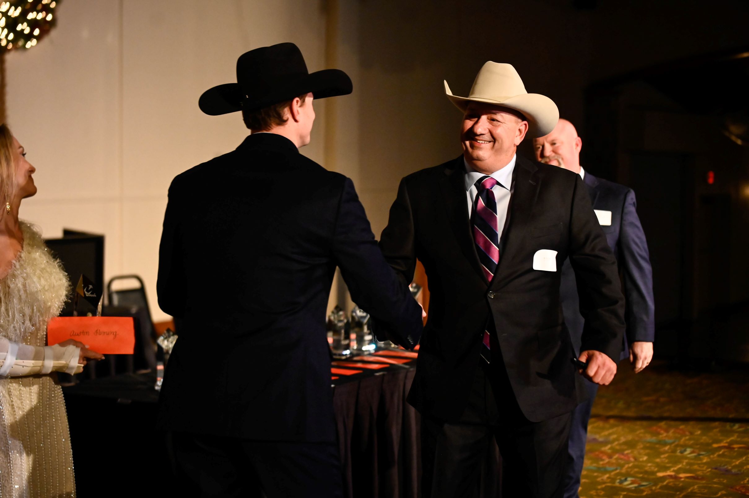 Two men in cowboy hats shaking hands at an indoor event.