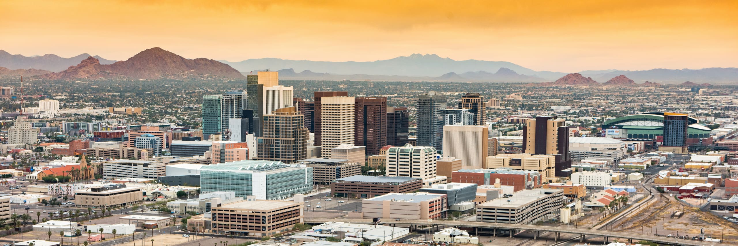 Phoenix cityscape with downtown skyline and mountain backdrop at sunset.