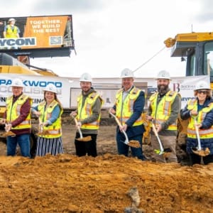 Group of construction workers and officials in safety gear participating in a groundbreaking ceremony.