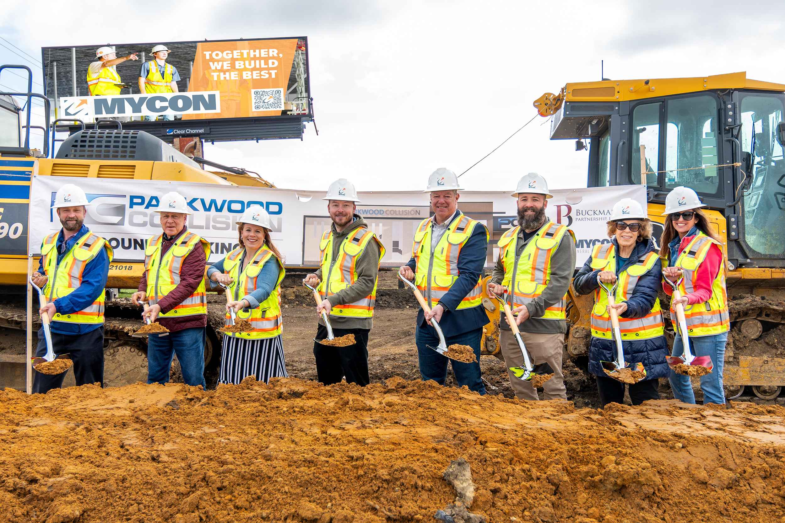 Group of construction workers and officials in safety gear participating in a groundbreaking ceremony.