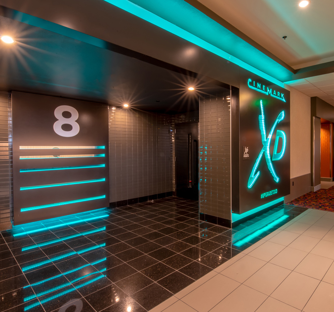 A modern cinema entrance with neon lights displaying "CineMark XD Auditorium" and a large number 8 on the wall, indicating the theater hall number.
