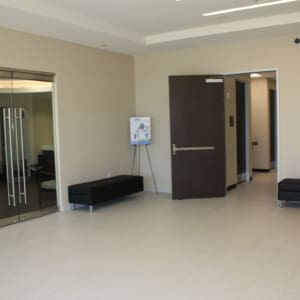A modern, empty lobby at Star Medical Center features beige tile floors, glass double doors, dark benches, an open door to a hallway, and a poster on an easel.