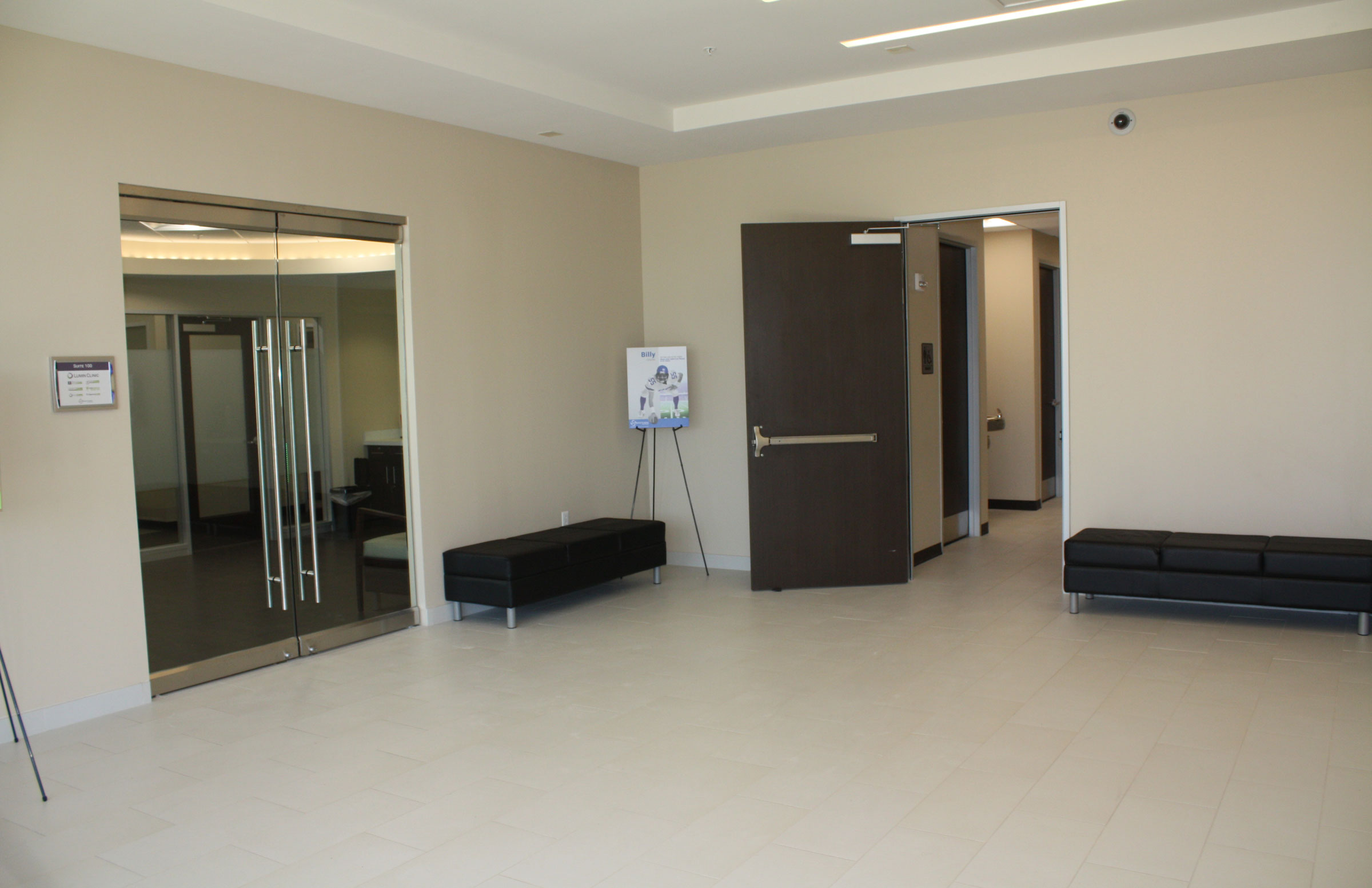 A modern, empty lobby at Star Medical Center features beige tile floors, glass double doors, dark benches, an open door to a hallway, and a poster on an easel.