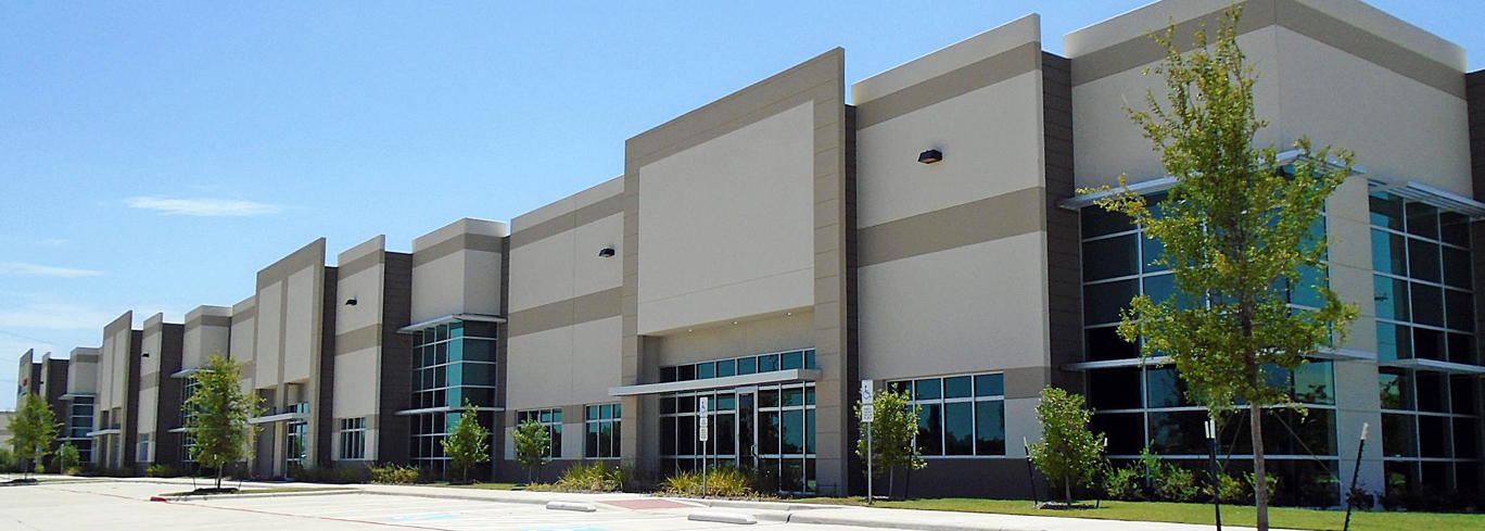 A modern, single-story commercial building with large windows and multiple entrances, set in a paved area with parking spaces and small trees in front.