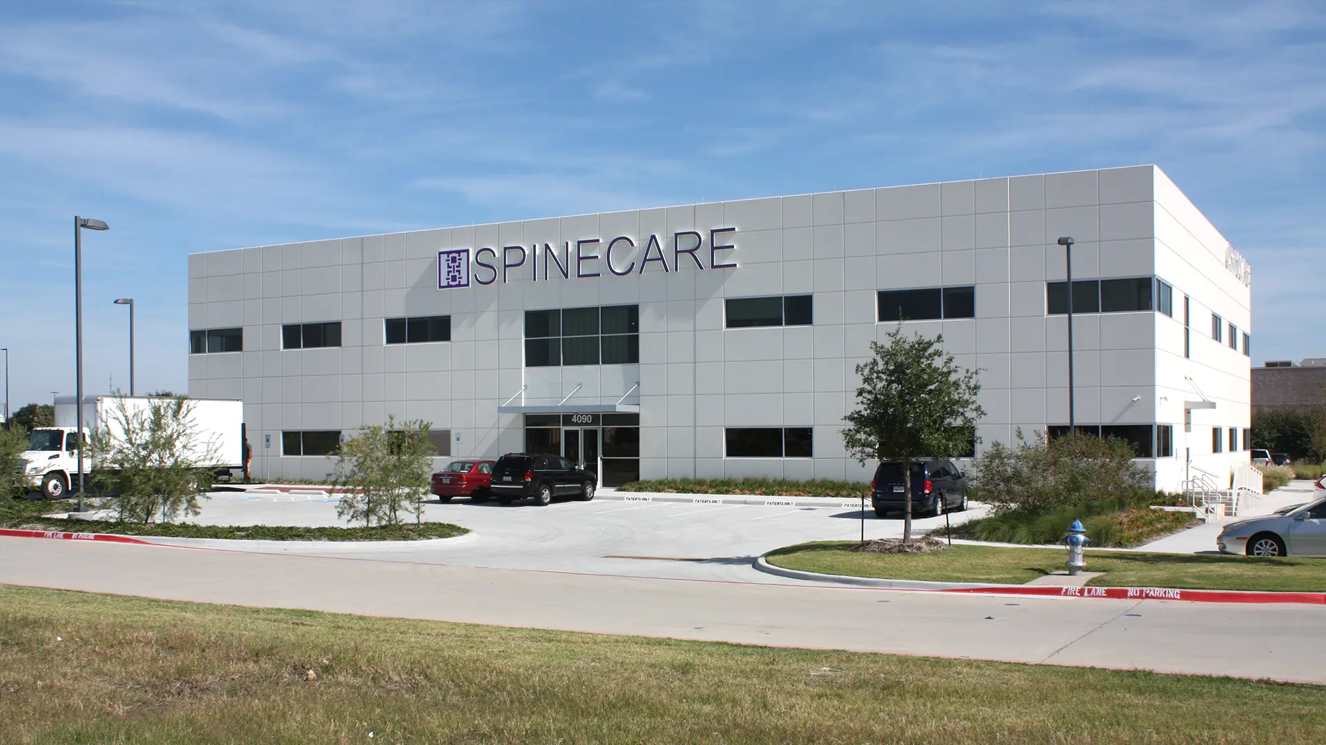 A two-story medical office building with "SpineCare" signage stands beside Star Medical Center, featuring a parking lot with several cars and a grassy area in the foreground.