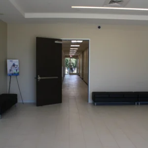 A spacious, empty hallway at Star Medical Center with tiled floors and beige walls, featuring black benches along the sides and an open door leading to a corridor bathed in natural light at the far end.