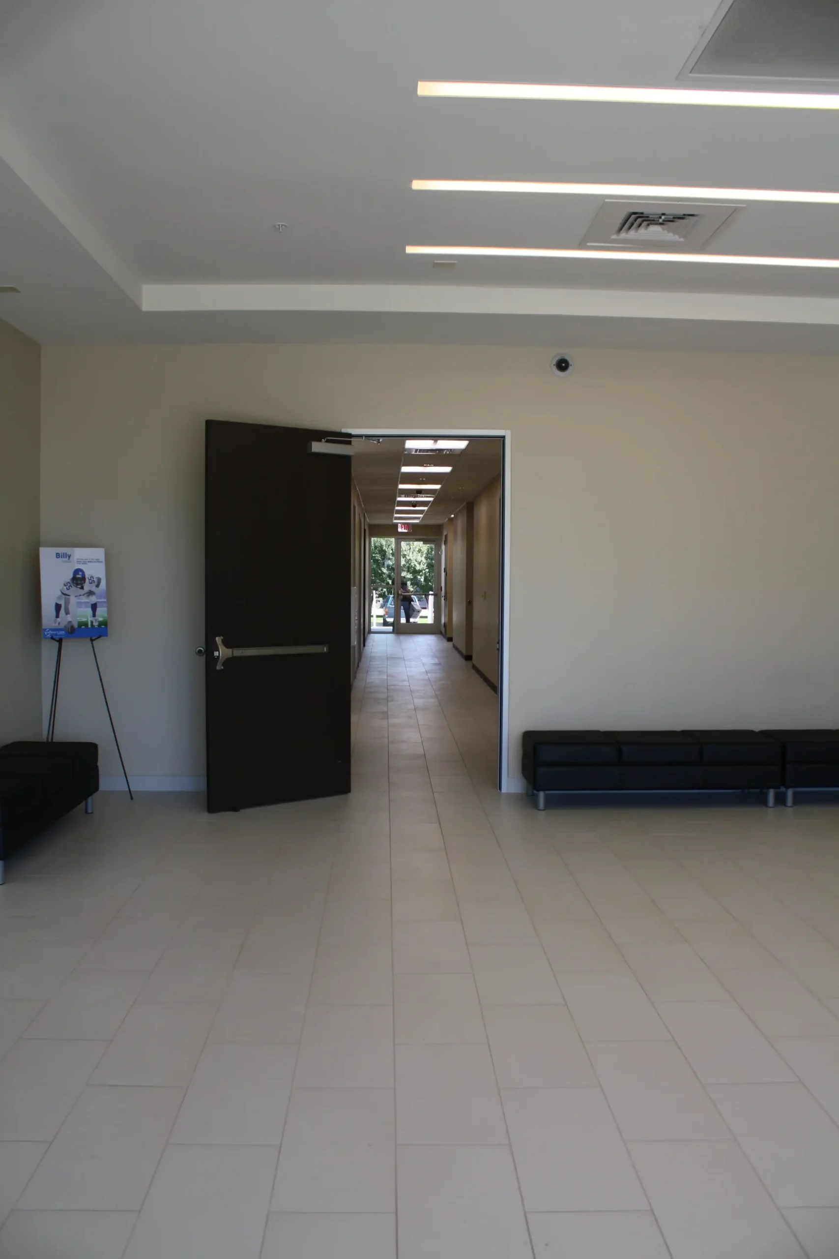 A spacious, empty hallway at Star Medical Center with tiled floors and beige walls, featuring black benches along the sides and an open door leading to a corridor bathed in natural light at the far end.