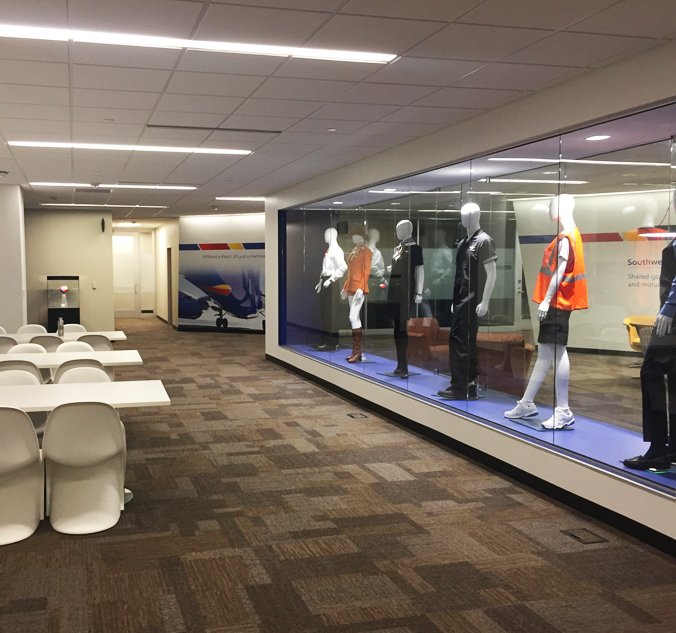 Museum exhibit displaying various airline crew uniforms in a modern, well-lit interior hall with tables and chairs on the left.