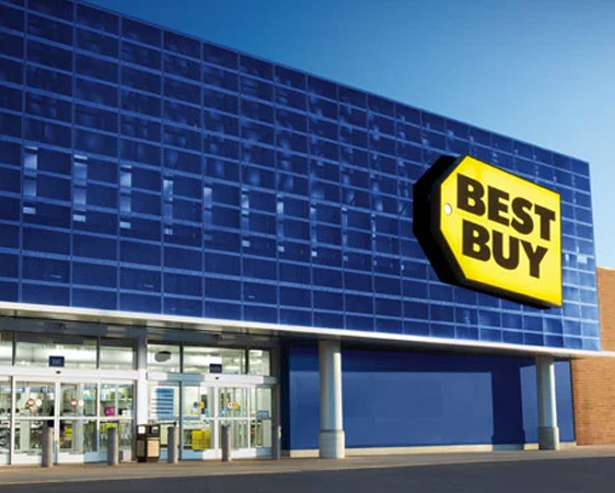 A large blue building with a prominent yellow "Best Buy" sign above the entrance. The entrance has glass doors and windows.