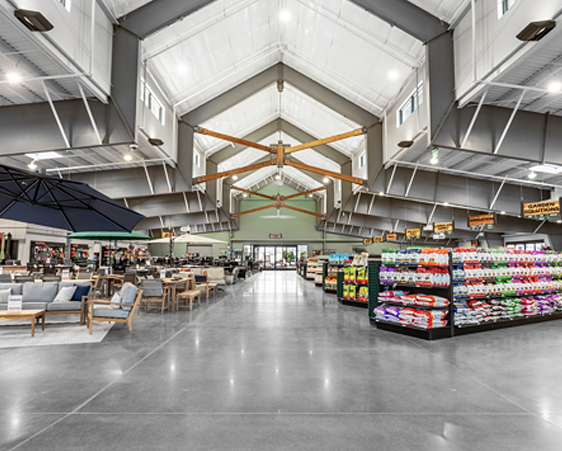 A spacious, well-lit store interior with high ceilings, showcasing outdoor furniture sets on the left and rows of pet supplies on the right.