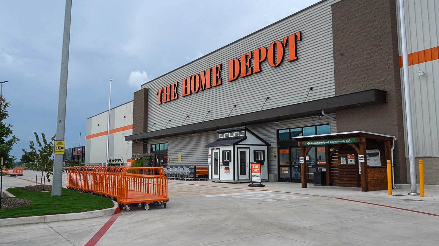 Exterior view of a Home Depot store with shopping carts lined up outside and a small shed displayed near the entrance.