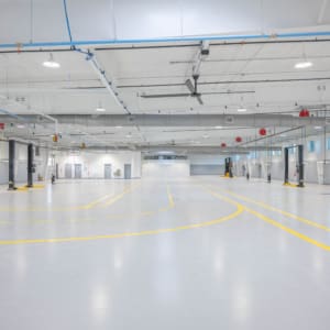 Spacious, empty industrial warehouse with high ceilings, white walls, yellow floor markings, and overhead lighting—ideal for Parkwood Collision Center Construction projects.