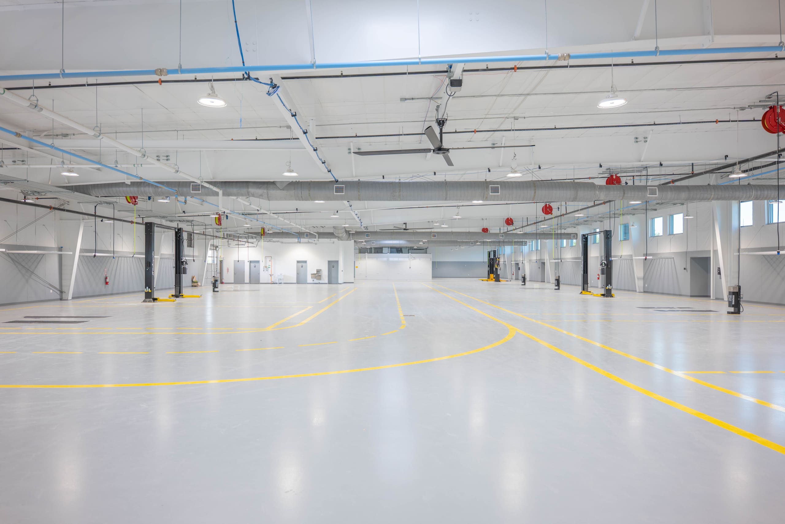 Spacious, empty industrial warehouse with high ceilings, white walls, yellow floor markings, and overhead lighting—ideal for Parkwood Collision Center Construction projects.