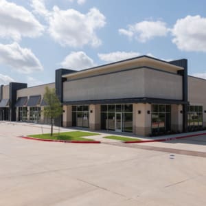 A modern, empty commercial strip mall building—ideal for ventures like Parkwood Collision Center Construction—with large windows and a spacious parking lot under a partly cloudy sky.