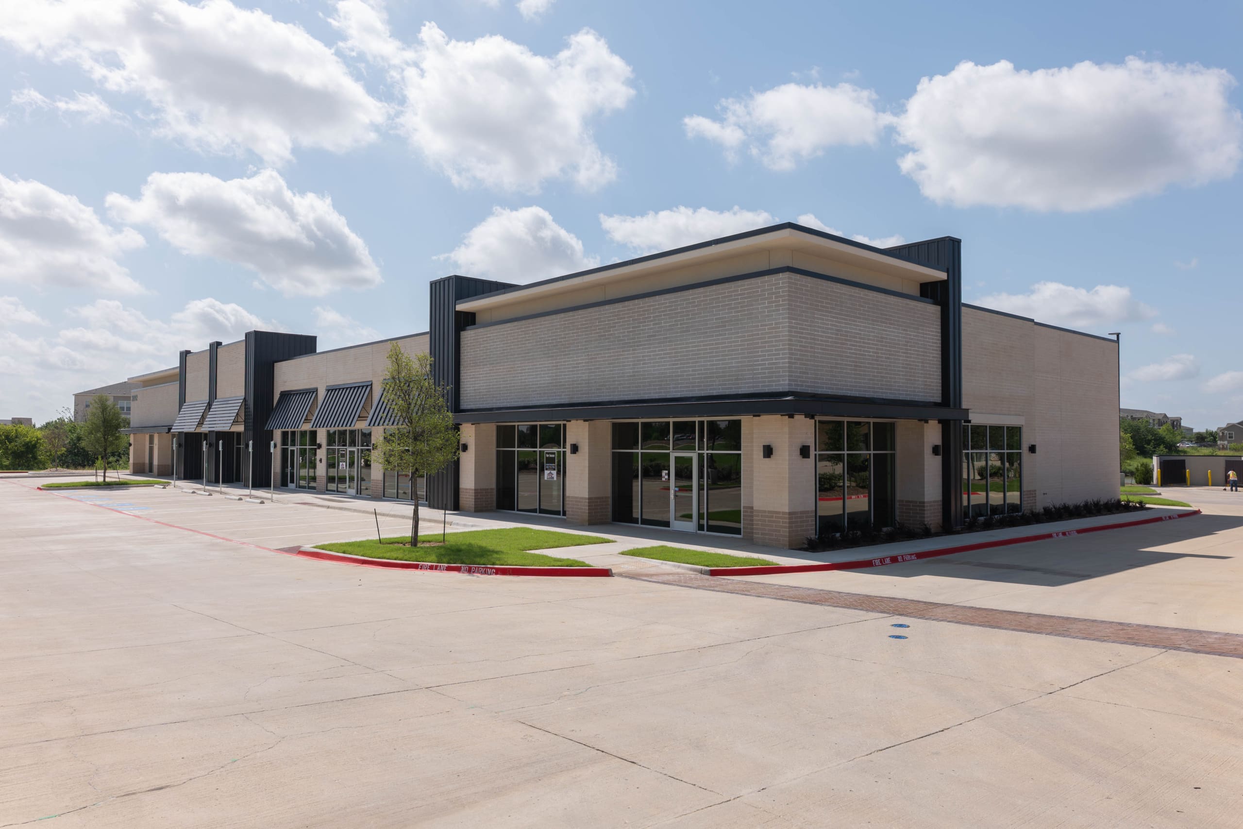 A modern, empty commercial strip mall building—ideal for ventures like Parkwood Collision Center Construction—with large windows and a spacious parking lot under a partly cloudy sky.