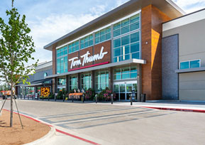 The image shows the exterior of a Tom Thumb grocery store with large windows, a tree, and clear skies in the background.