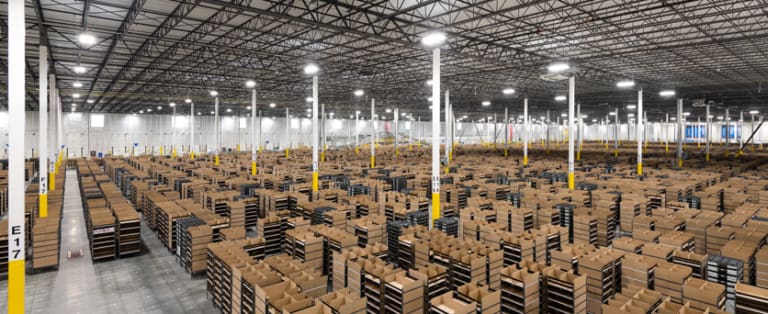 Interior of a large warehouse filled with rows of brown cardboard boxes stacked on shelves, under a high ceiling with numerous lights.