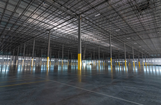 Empty industrial warehouse interior with a vast open floor, high ceilings, and metal support beams.