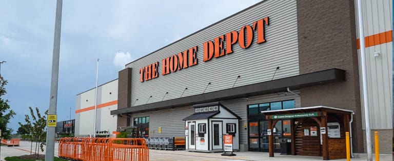 Exterior view of a Home Depot store with orange signage and an outdoor display of sheds and carts.