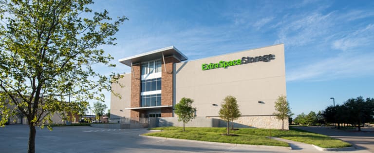 A large Extra Space Storage facility with a modern design, surrounded by a few trees and a clear blue sky.