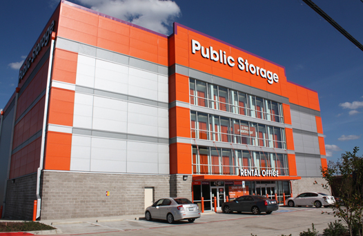 A large orange and gray Public Storage building with a rental office entrance and several cars parked in front.