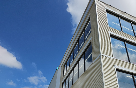 A modern building with large windows is seen against a blue sky with a few clouds.