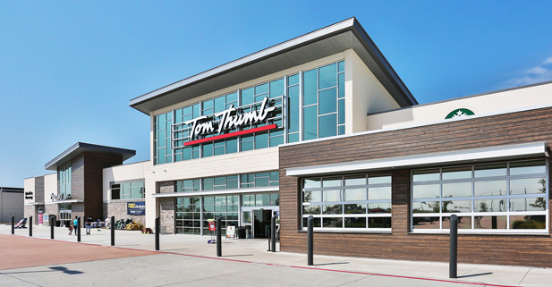 Exterior view of a grocery store with large glass windows, a prominent sign, and a clear blue sky above.