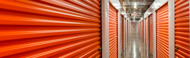 A hallway of an indoor storage facility with bright orange roll-up doors on both sides and a shiny concrete floor.