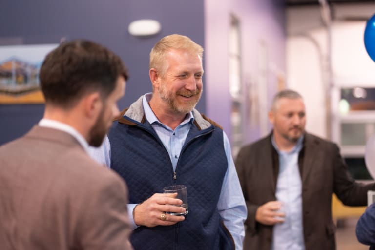 A group of men in casual and business attire talking and holding drinks at an indoor gathering.