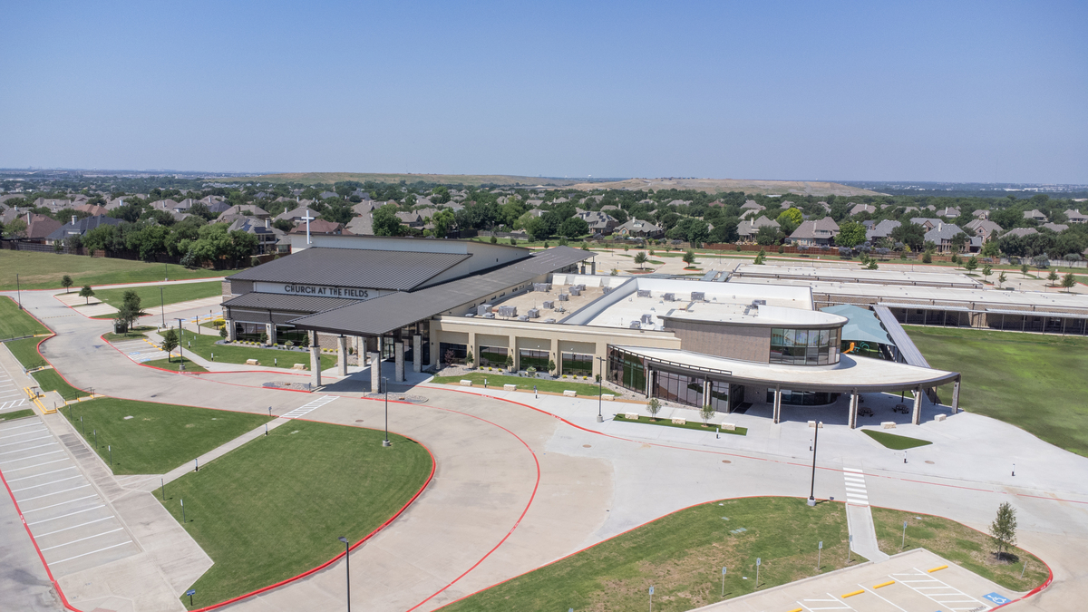 Aerial view of a large modern church building with adjacent parking lots, surrounded by green lawns and residential neighborhoods.