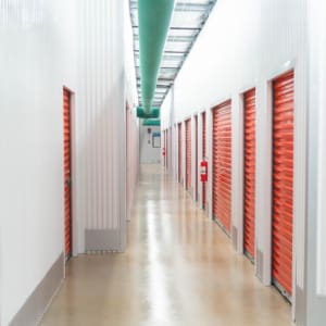 A brightly lit hallway at U-Haul of East Denton Construction features rows of orange roll-up doors on both sides and a polished floor.
