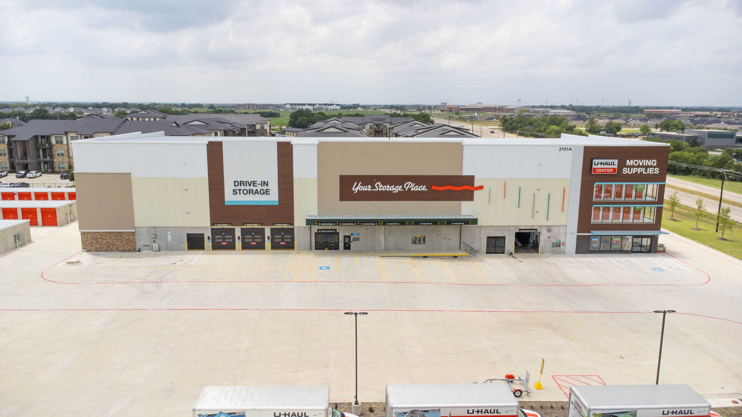 A large self-storage facility with drive-in storage, moving supplies, and U-Haul services by U-Haul of East Denton Construction, surrounded by a paved parking lot and nearby apartments.