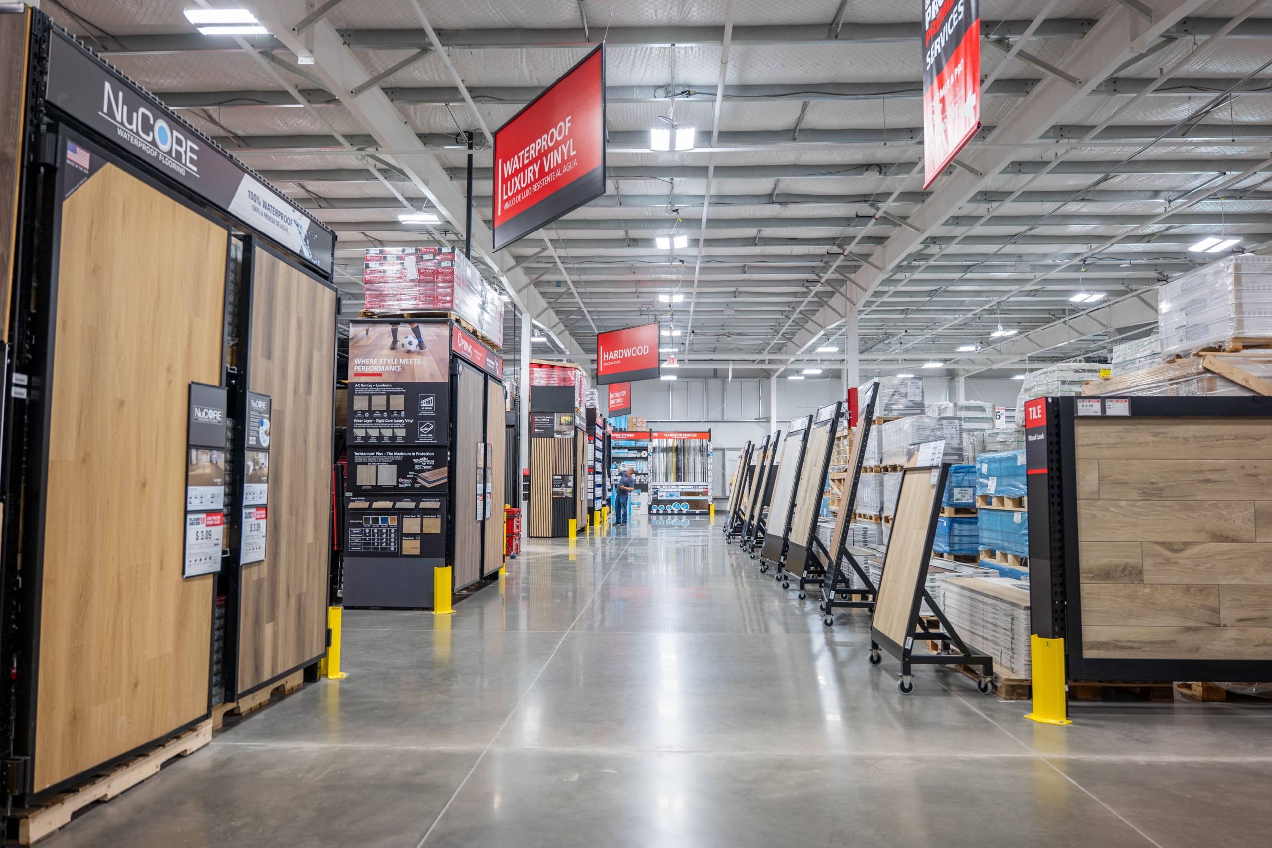 A wide aisle in Home Depot San Antonio West displays various flooring samples and materials, with shelves and signage visible under bright lighting.