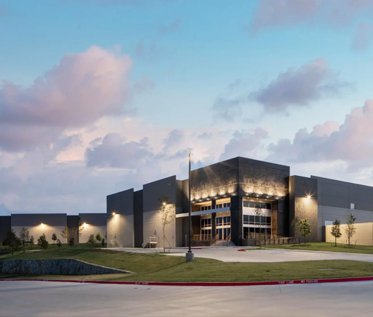 A modern, angular building with large glass entrance showcases retail construction expertise, surrounded by grass and young trees under a partly cloudy sky at dusk.